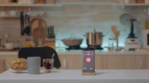 Phone with intelligent software placed on table in kitchen with nobody in, controlling light with high tech application. Mobile with smart home app in empty house automation system
