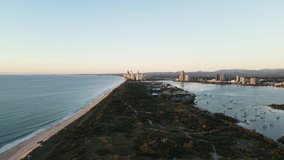 Coastal nature parklands dividing a boat harbor and coastline with an urban city skyline rising above in the foreground. High revealing panoramic drone view