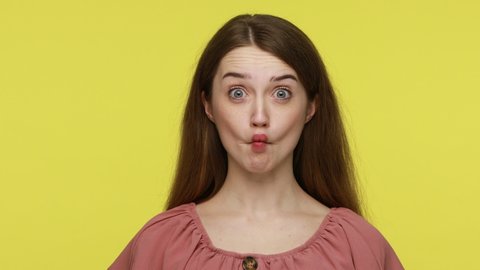 Funny young woman wearing elegant dress making fish face with pout lips and looking big eyes, amazed expression, having idiotic foolish expression .Indoor studio shot isolated on yellow background.