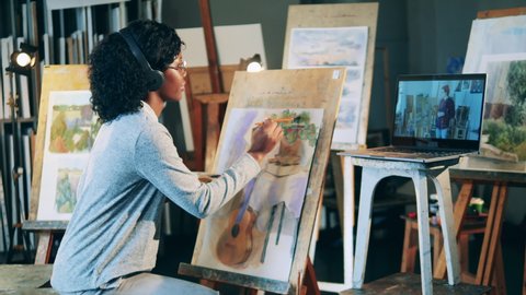 African ethnicity lady is painting while having a video lesson Stockvideó