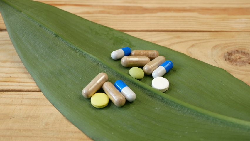 Herb pills and capsule with syringe on fresh green leaf background, Nutritional Supplement, Alternative Medicine concept