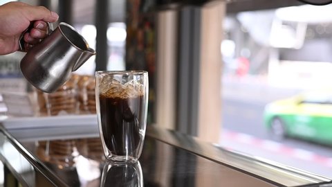 slow motion barista pouring milk into a glass of iced coffee