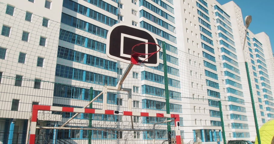 On the playground in the courtyard of a large residential building there are football gates and a basketball ring.