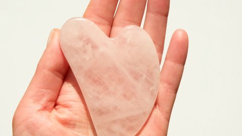 Gua Sha Rose Quartz Scraper. Gua Sha stone for face and neck massage. Gua sha scraper in the shape of a heart in a female hand
