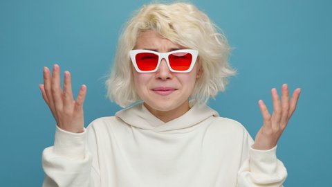 Surprised asian woman face Shows Emotion What a fuck? Gesturing with his hands in front of camera sunglasses with delight and admiration on blue background. Emotions People concept. Lifestyle. Freedom