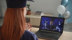 female student in academic dress rejoices at received diploma online live broadcast of ceremony for graduates via video link on laptop