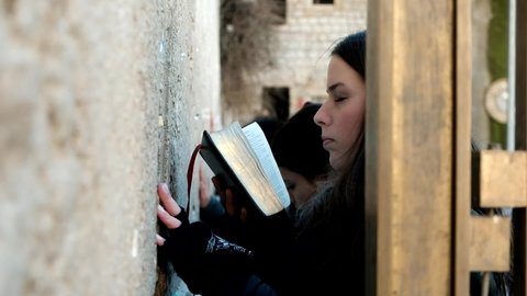 A pretty, young lady, is praying and holding a Bible in front of the Wailing Wall, when done, she is looking up towards the sky, January 8th, 2019, old city of Jerusalem, Israel.