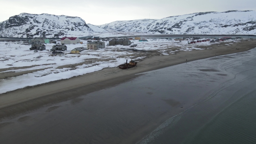 Aerial Top view of old wrecked fishing ships drowned at the sea shore in snowy winter season. Footage. Aerial view of the ruined boat in the cold water of Barents sea in Teriberka, Russia