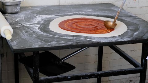 The process making pizza, base dough greased with tomato sauce. Cooking Italian food