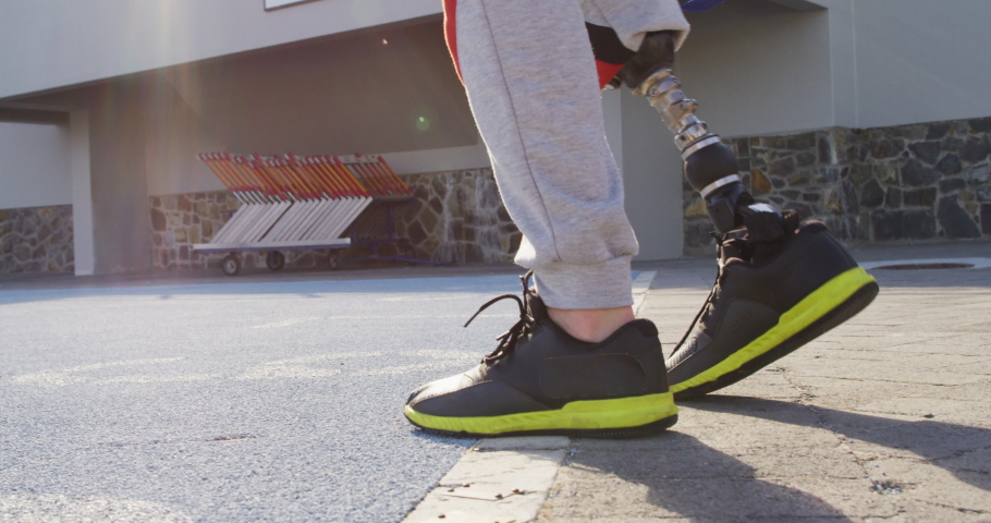 Back view of caucasian disabled male athlete with prosthetic leg walking. professional runner training at sports stadium.