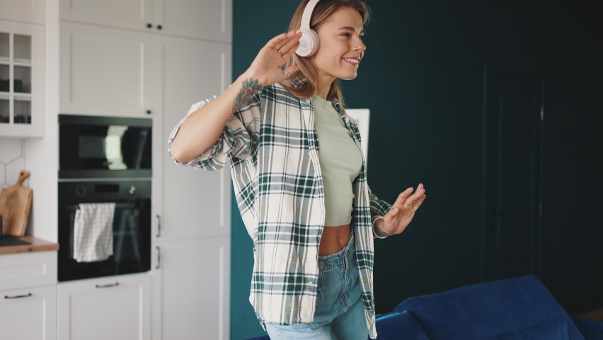 Fun time. Young blonde lady relaxing at home, listening to music in wireless headphones and dancing, enjoying free time, slow motion