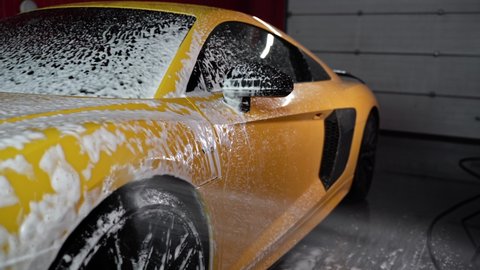 ROSTOV-ON-DON, RUSSIA - MARCH 28, 2021: Cleaning the bright yellow Audi R8 sports car with white foam shampoo. Spraying white foam on to sports car. Car wash.