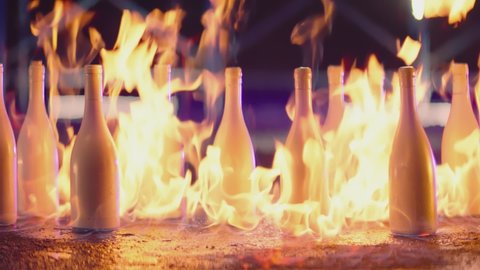 Many white bottles burning on fire .  Wine or champagne bottles burn on flame on the floor . Beautiful , abstract , creative scene for video clips  .  Evening or night shot in slow motion . Close up 