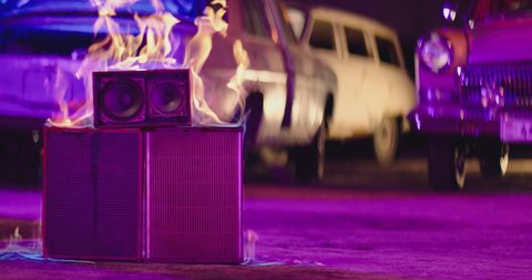 4K Scene of burning speaker in abandoned garage . Purple and blue lights . Speaker is burning on the concrete floor in the street . Fire burning in slow motion . Vintage and retro style . 