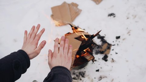 A homeless man has built a fire in the snow and warms his hands over the fire. Close-up view from above