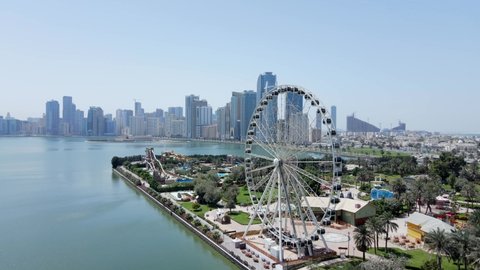 4K: Aerial view of Sharjah's Khalid Lake with city skyline and Eye of Emirates on a bright sunny day, United Arab Emirates