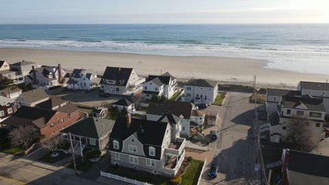 Aerial fly over of houses leading to beach with lone person walking with dog. Drone forward motion.