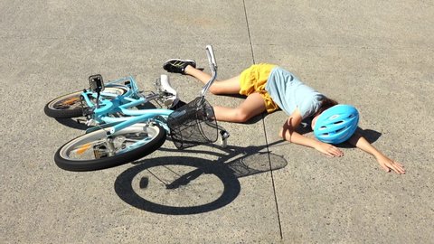 Young girl fallen of a bicycle laying down beside her bike unconscious on a concreat paved road. Real people. Copy space