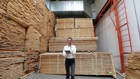 Business woman walking in the carpentry factory talking on the phone and using tablet pc. Carpentry factory. Factory for the production of parquet board

