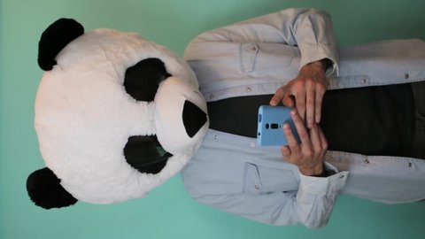 Excited man in panda mask reading good news on mobile phone on blue trendy color background. Vertical video format view screen for social media