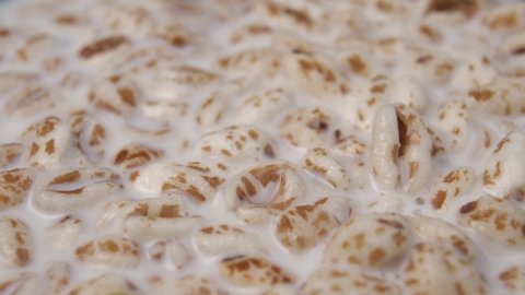 Puffed spelt wheat flakes fall into a bowl of cereal milk porridge. Slow motion. Macro photography
