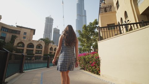 Woman walking through luxury apartment complex near Burj Khalifa skyscraper in Dubai. Low angle view of tourist exploring metropolitan city center of Dubai, UAE in 2021