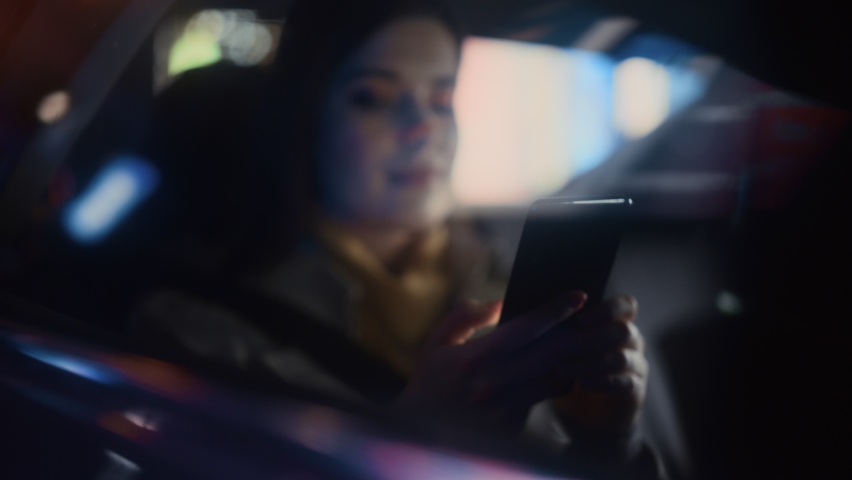 Stylish Female is Commuting Home in a Backseat of a Taxi at Night. Beautiful Woman Passenger Using Smartphone and Looking Out of Window while in a Car in Urban City Street with Working Neon Signs. Royalty-Free Stock Footage #1072002682