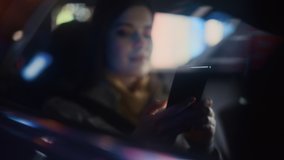 Stylish Female is Commuting Home in a Backseat of a Taxi at Night. Beautiful Woman Passenger Using Smartphone and Looking Out of Window while in a Car in Urban City Street with Working Neon Signs. - Powered by Shutterstock - Get 15% off with code: PIKWIZARD15