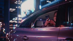 Excited Female is Looking Out of the Window from Backseat of a Car at Night. Woman Taking Photos and Videos on a Smartphone with Amazement of How Beautiful is the City Street with Working Neon Signs.