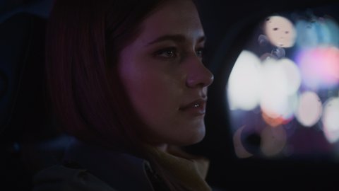Close Up Portrait of a Female Commuting Home in a Backseat of a Taxi at Night. Beautiful Woman Passenger Looking Out of Window while in a Car in City Street with Working Neon Signs. Cinematic Footage.