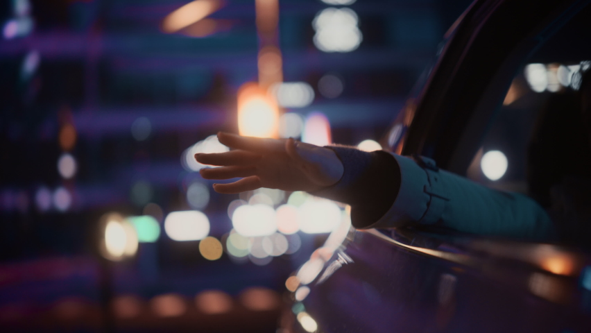 Female is Commuting Home in a Backseat of a Taxi at Night. Passenger Chilling and Holding Her Hand Outside of Window while in a Car in Urban City Street with Working Neon Signs. Cinematic Footage. | Shutterstock HD Video #1072002973