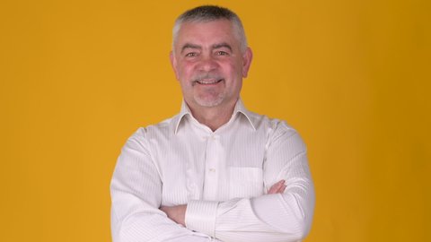 Portrait of a Cheerful elderly gray-haired man smiling and looking at the camera against a yellow studio background. People lifestyle concept.	