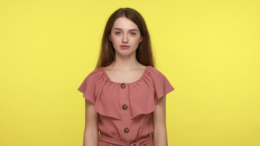 Smiling attractive female wearing pink dress holding plush bear in hands, being happy receives cute gift, expressing optimism and joy, boasting her present. Indoor shot isolated on yellow background.