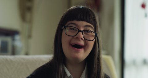 Authentic macro of happy friendly teen girl with down syndrome is smiling in camera at home. Concept of handicapped, child care, healthcare,disability, people, optimism