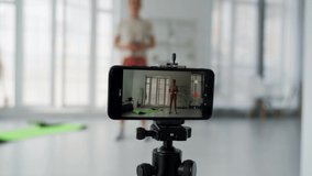 The girl shoots her fitness video blog on a smartphone. The girl conducts distance fitness training online. The girl shoots a video blog during fitness. Physical exercises.