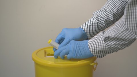 A man wearing blue protective gloves carefully disposing of a big syringe into a yellow medical waste container