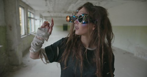 Mad woman interacting with virtual reality in glasses. Crazy female scientist with messy hair and in steampunk handmade goggles glowing with neon lights standing in old building and touching air while