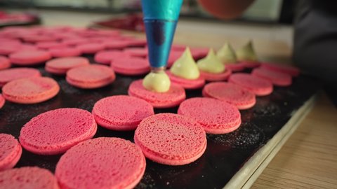 Process Of Making macaroon at home. Shot of hands of female pastry chef holding white macaron with ganache and squeezing red fruit jam from bag. Nature pastry macaroons. High quality 4k footage