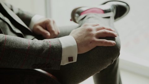 Man in red socks and business suit is sitting leg by leg and straightens the lapel of his jacket