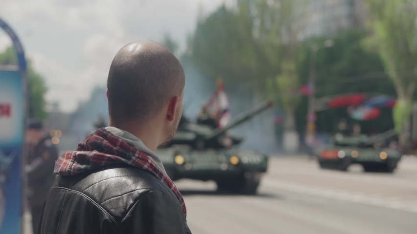 A man watches tanks moving through the city during a military parade
