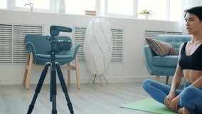Young sportswoman recording video for internet vlog sitting on yoga mat and exercising concentrated on creative activity. People and vlogging concept.