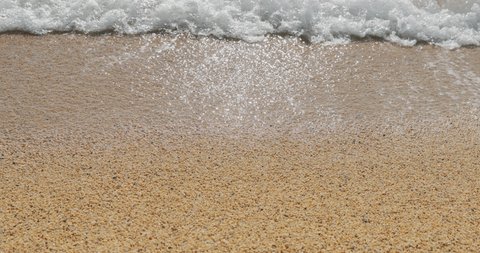 Close-up slow motion footage of beach of gravel, the coarse sand, waves run on sand, wet stones glint in the sun, sun reflection on water