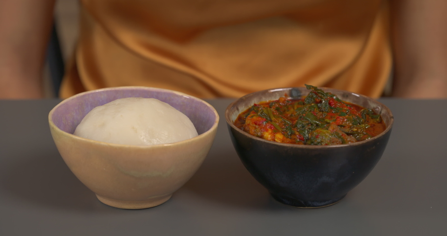 Two bowls with west african traditional dishes. Woman is eating Ogbono soup and fufu using her fingers. Nigerian cuisine. Royalty-Free Stock Footage #1072025680