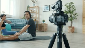 Male and female vloggers are working out on yoga mats recording video for internet vlog at home. Contemporary activity and influencers concept.