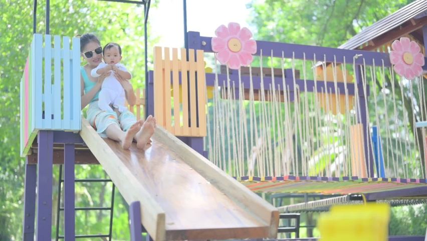 Happy asian kid boy and mother having fun and sliding on outdoor playground . Child smiling. Summer leisure for kids.