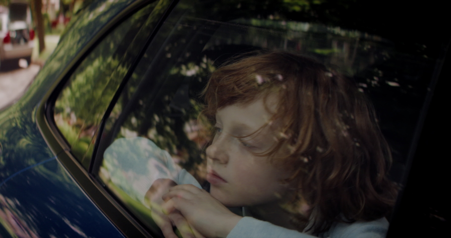 CU Portrait of cute bored little kid boy looking through closed car window while riding through neighborhood. Shot with 2x anamorphic lens