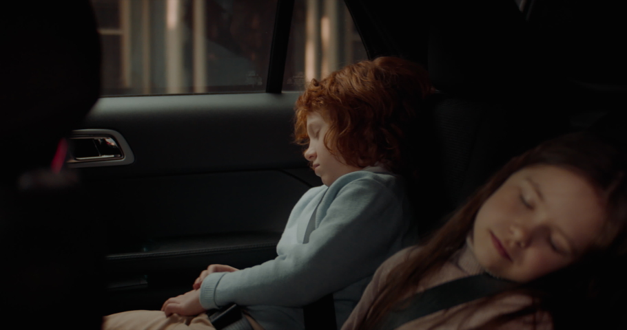 Cute little siblings sleeping on a back seat of a modern SUV while riding through neighborhood. Shot with 2x anamorphic lens Royalty-Free Stock Footage #1072027921