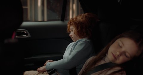 Cute little siblings sleeping on a back seat of a modern SUV while riding through neighborhood. Shot with 2x anamorphic lens