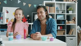 Kid and father mixed race family are recording content for internet vlog talking about playdough using smartphone camera at home. Blogging and influencers concept.