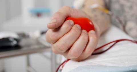 Close up of blood donor squeezing rubber bulb in form of heart in hand. Cropped shot of volunteer in hospital donating blood. Person during blood donation procedure